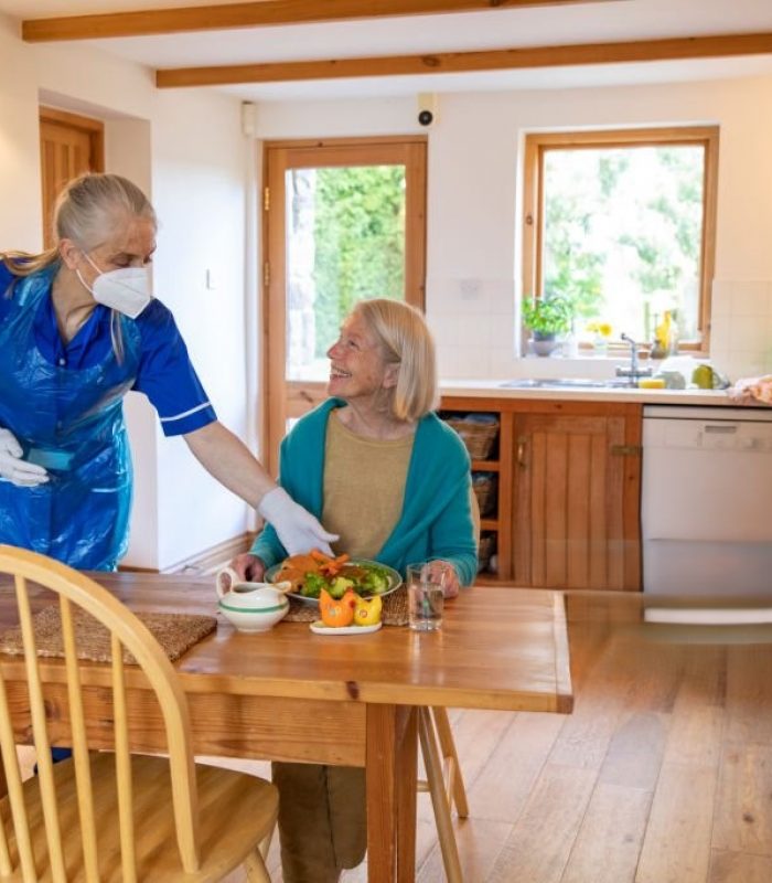 A frontline worker puts down her senior client who is shieldings food and is keeping safe during the coronavirus pandemic by wearing her PPE consisting of mask, gloves, apron making sure to keep a practical distance.